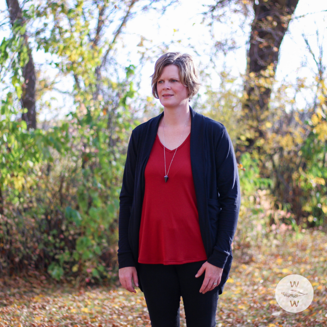Woman wearing black jeans, red essential basic tank top, with a cozy long black cardigan. The setting is fall/autumn and it's a good time to get into capsule wardrobes because they're so easy to layer and keep warm, while being comfortable and fashionable.