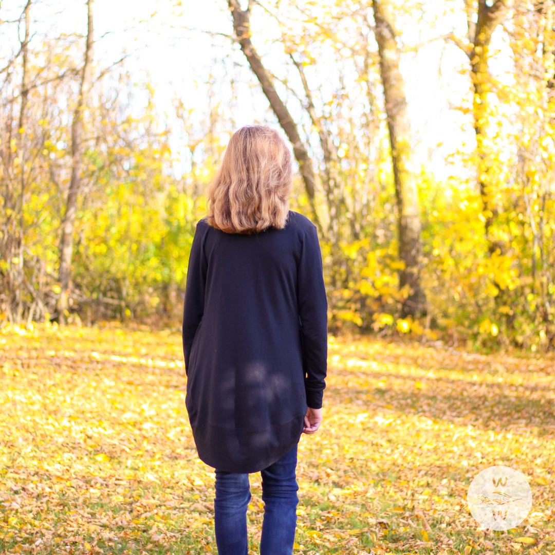 Girl wearing blue jeans, red essential basic tank top, with a cozy long black cardigan. The setting is fall/autumn and it's a good time to get into capsule wardrobes because they're so easy to layer and keep warm, while being comfortable and fashionable.