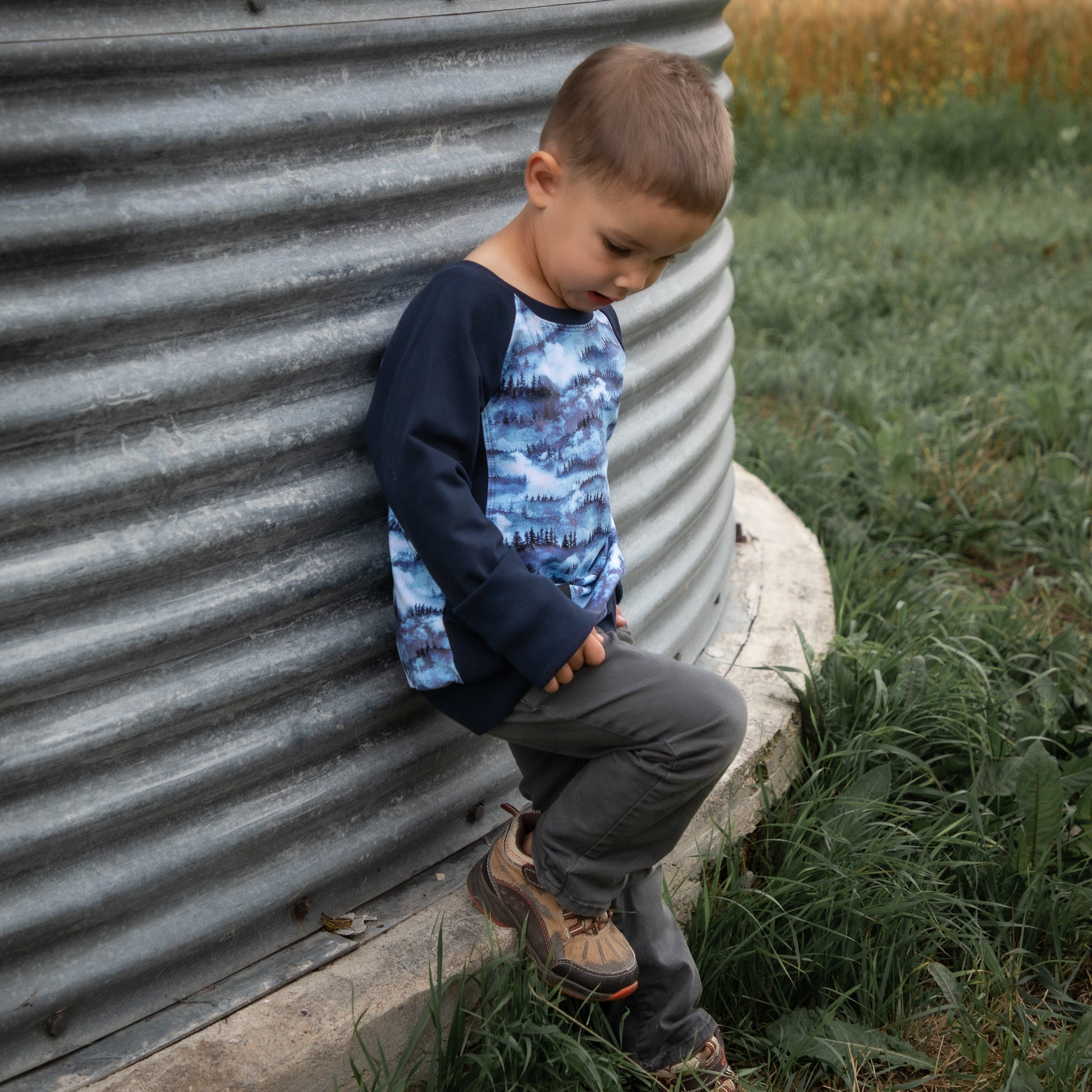 Child sitting against a metal silo in a rural setting with a field in the background