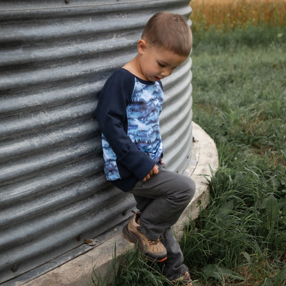 Child sitting against a metal silo in a rural setting with a field in the background