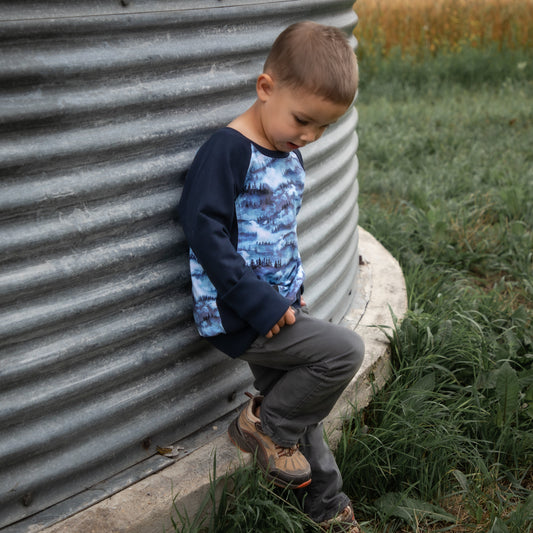 Child sitting against a metal silo in a rural setting with a field in the background