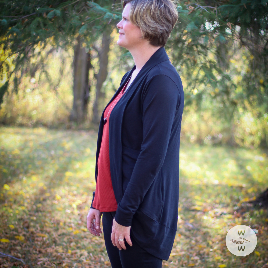 Woman wearing black jeans, red essential basic tank top, with a cozy long black cardigan. The setting is fall/autumn and it's a good time to get into capsule wardrobes because they're so easy to layer and keep warm, while being comfortable and fashionable.