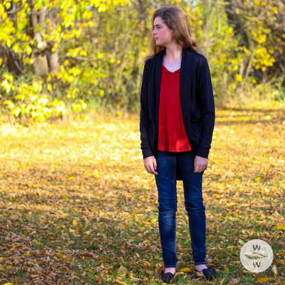 Girl wearing blue jeans, red essential basic tank top, with a cozy long black cardigan. The setting is fall/autumn and it's a good time to get into capsule wardrobes because they're so easy to layer and keep warm, while being comfortable and fashionable.